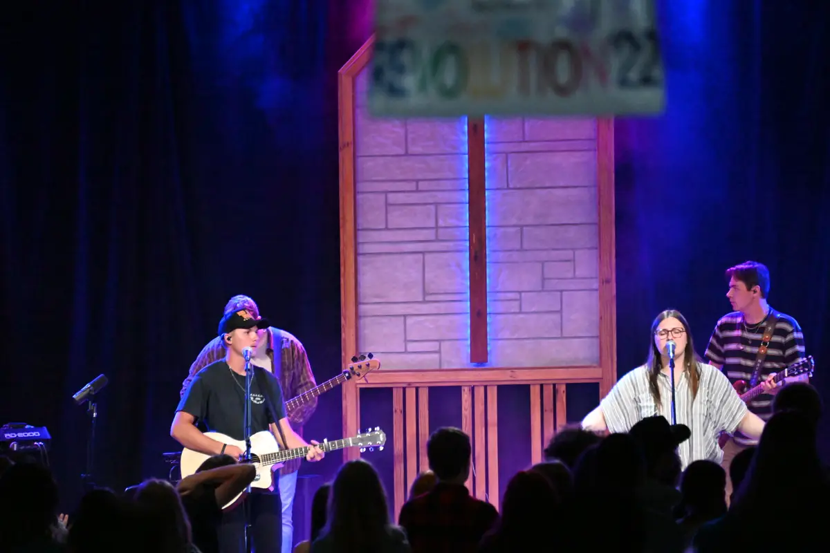 Evening worship at teen camp, a band on the lit stage in front of a standing crowd